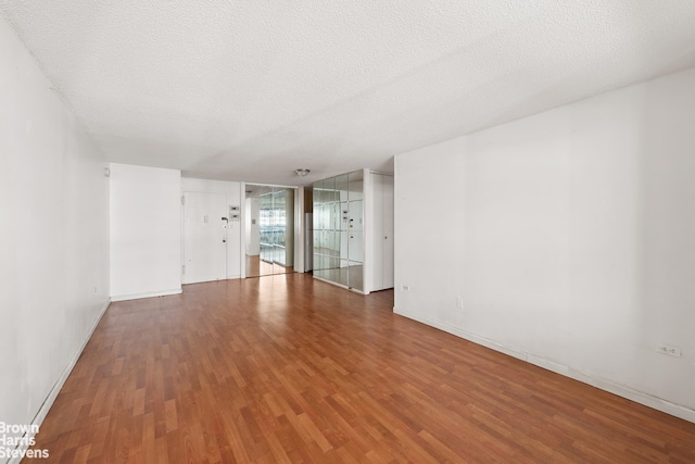 spare room with baseboards, a textured ceiling, and wood finished floors