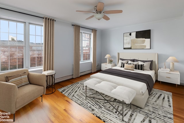 bedroom featuring ceiling fan, ornamental molding, baseboard heating, and wood finished floors