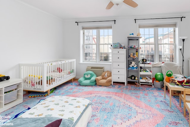 bedroom featuring a nursery area, ornamental molding, a ceiling fan, and wood finished floors
