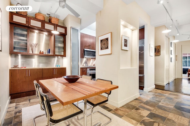 dining space featuring rail lighting, baseboards, ceiling fan, and stone tile floors