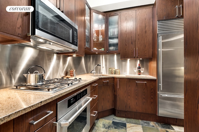 425 Park Ave S Unit 2C, New York City, NY 10016 - kitchen featuring appliances with stainless steel finishes, a sink, light stone countertops, and glass insert cabinets
