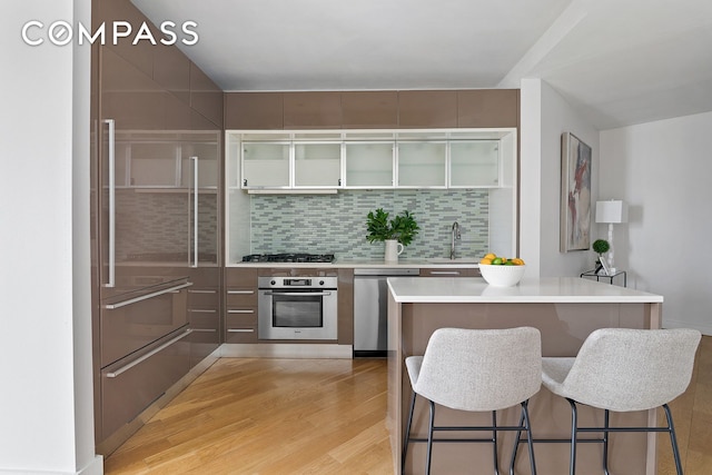 75 Wall St Unit 36F, New York City, NY 10005 - kitchen featuring stainless steel appliances, light countertops, light wood-style flooring, a breakfast bar, and tasteful backsplash