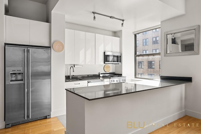 99 John St Unit 2006, New York City, NY 10038 - kitchen featuring stainless steel appliances, light wood-style flooring, white cabinetry, and dark countertops