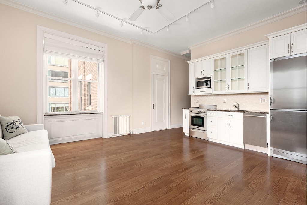 kitchen with built in appliances, track lighting, glass insert cabinets, dark wood-style floors, and crown molding