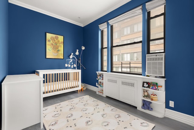 bedroom with baseboards, a crib, wood finished floors, crown molding, and cooling unit
