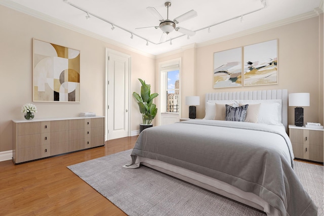 bedroom with rail lighting, ornamental molding, light wood-type flooring, and baseboards