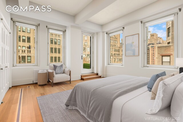 bedroom with baseboards, beam ceiling, radiator, and light wood-style floors