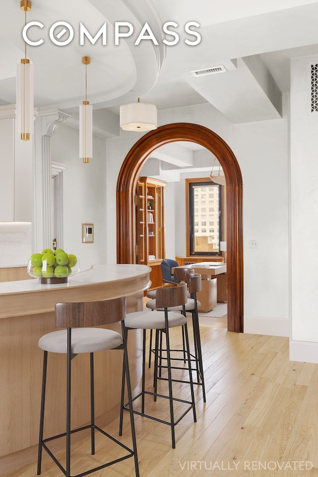 bar featuring visible vents, arched walkways, hanging light fixtures, baseboards, and light wood-style flooring