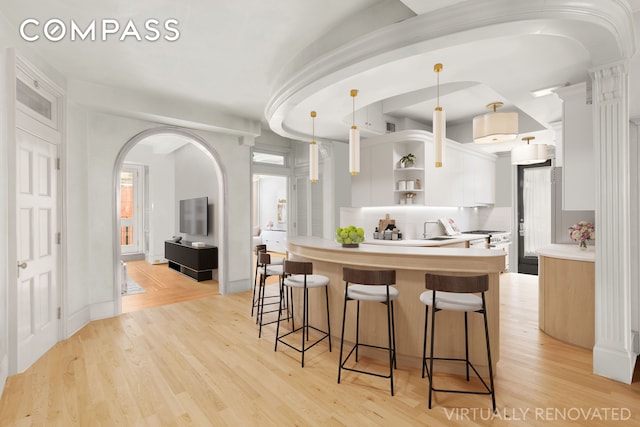kitchen featuring open shelves, a breakfast bar area, light countertops, white cabinets, and arched walkways