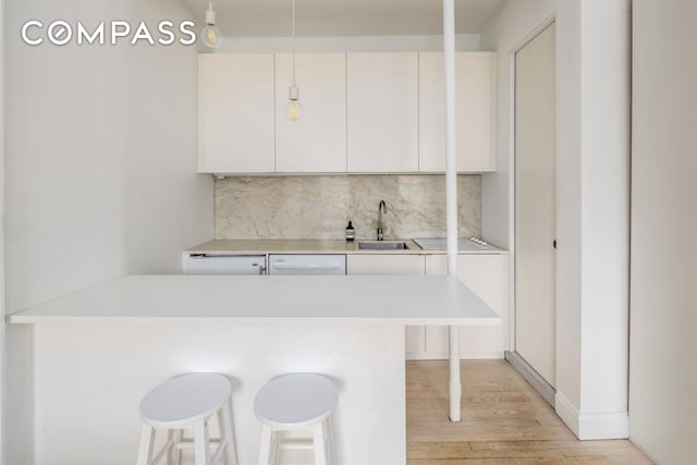 345 W 4th St Unit 8, New York City, NY 10014 - kitchen with a sink, a kitchen bar, light wood-style floors, backsplash, and white dishwasher