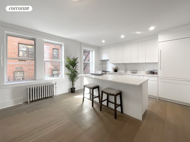 148-09 Northern Blvd Unit 1J, New York City, NY 11354 - kitchen featuring radiator heating unit, a sink, a kitchen island, a breakfast bar area, and modern cabinets