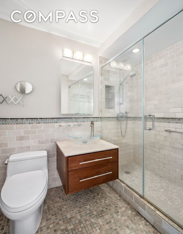 full bath with tile walls, toilet, a shower stall, vanity, and a wainscoted wall