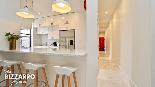 kitchen featuring a peninsula, white cabinetry, high quality fridge, and light wood finished floors