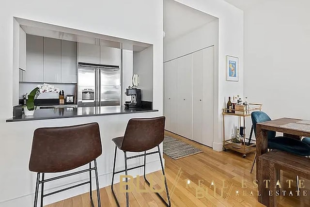 99 John St Unit Ph-9, New York City, NY 10038 - kitchen featuring stainless steel built in refrigerator, gray cabinets, dark countertops, light wood-style flooring, and a breakfast bar area
