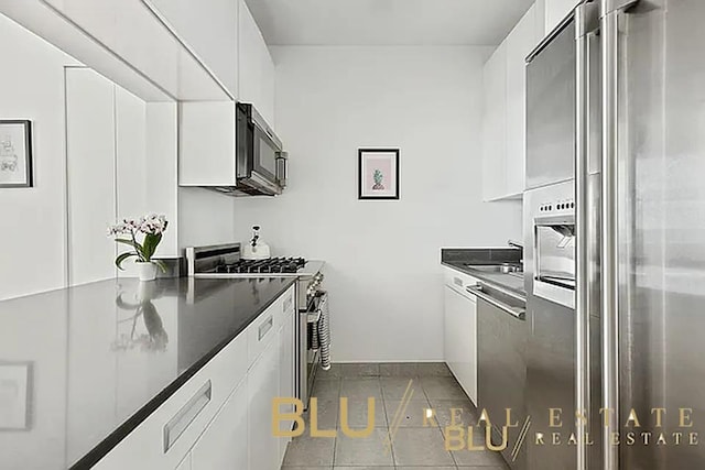 99 John St Unit Ph-9, New York City, NY 10038 - kitchen featuring stainless steel appliances, dark countertops, white cabinetry, dark tile patterned flooring, and modern cabinets