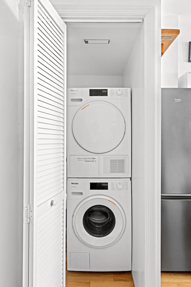 clothes washing area with stacked washer and clothes dryer, wood finished floors, and laundry area