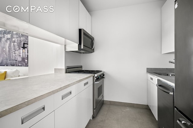 99 John St Unit 522, New York City, NY 10038 - kitchen with stainless steel appliances, baseboards, a sink, white cabinets, and light tile patterned flooring