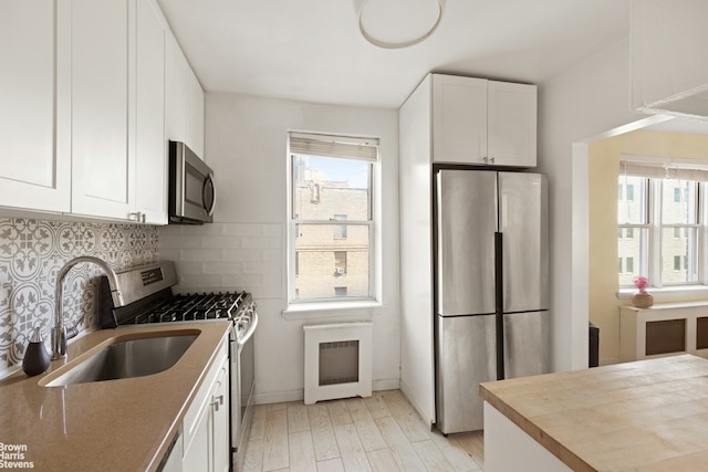 kitchen with appliances with stainless steel finishes, a sink, white cabinetry, light wood finished floors, and backsplash