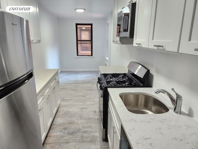kitchen with stainless steel appliances, a sink, light wood-style floors, and white cabinets