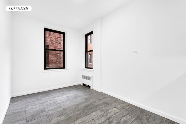 spare room featuring radiator heating unit, wood finished floors, and baseboards