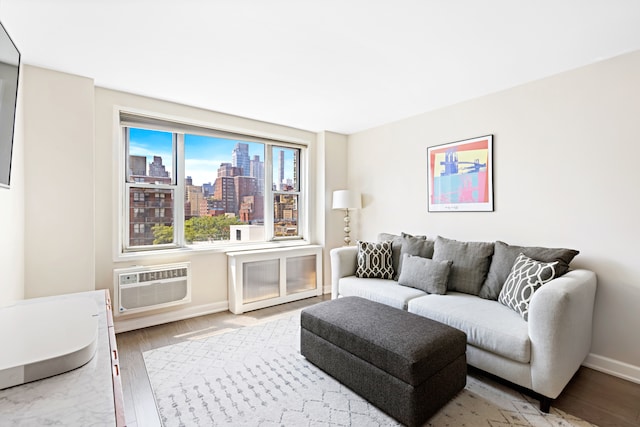 living room with an AC wall unit, a view of city, baseboards, and wood finished floors