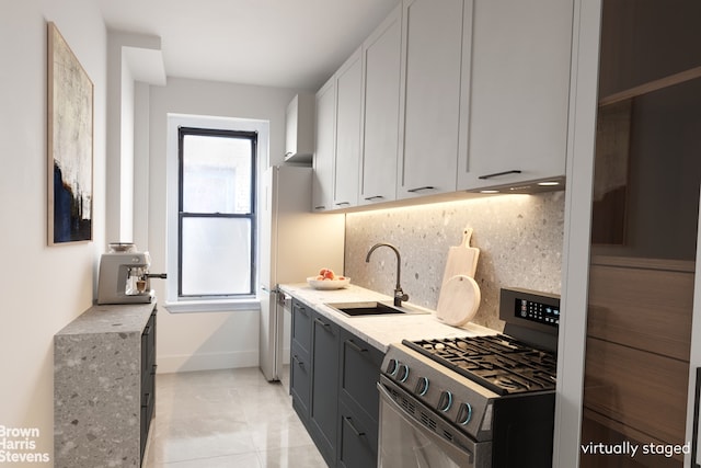 kitchen featuring baseboards, stainless steel gas range oven, white cabinetry, a sink, and backsplash