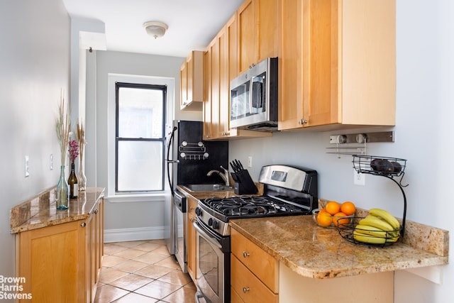 kitchen with a sink, light tile patterned floors, baseboards, and stainless steel appliances