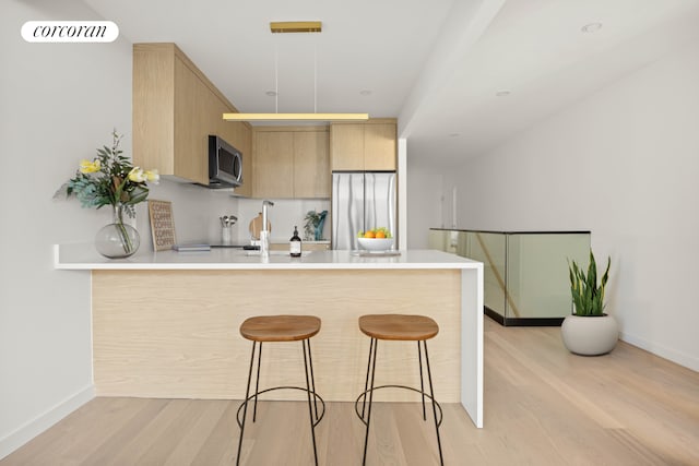 kitchen with stainless steel appliances, a peninsula, a kitchen bar, light wood-style floors, and light brown cabinets