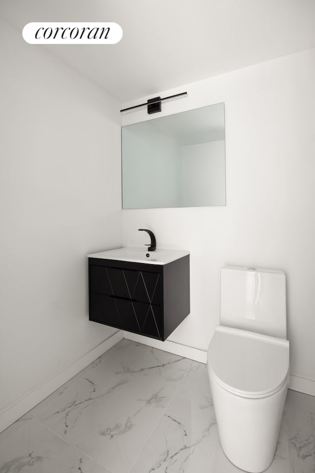 half bathroom featuring baseboards, marble finish floor, vanity, and toilet