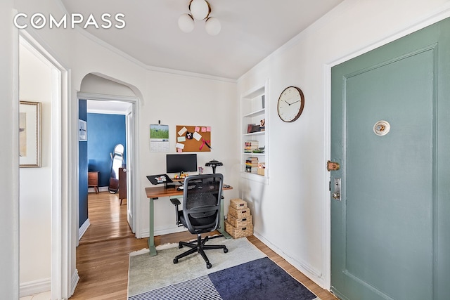 office area featuring built in shelves, arched walkways, ornamental molding, and light wood-style flooring