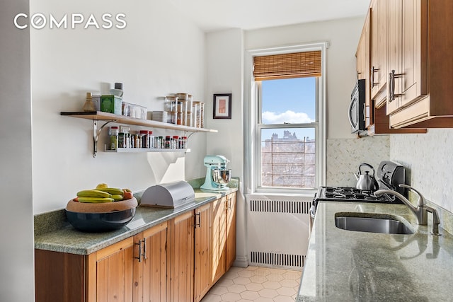 kitchen featuring a sink, stone countertops, radiator heating unit, stainless steel microwave, and backsplash