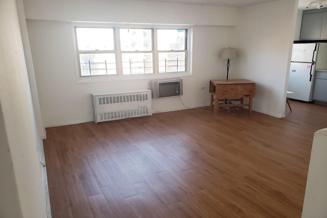 spare room featuring baseboards, wood finished floors, a wall unit AC, and radiator
