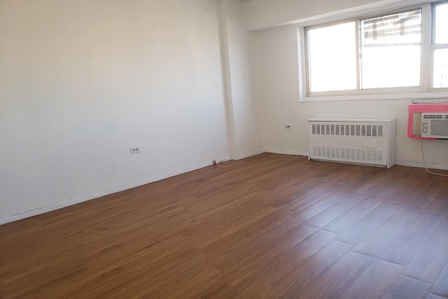 spare room with baseboards, wood finished floors, and radiator