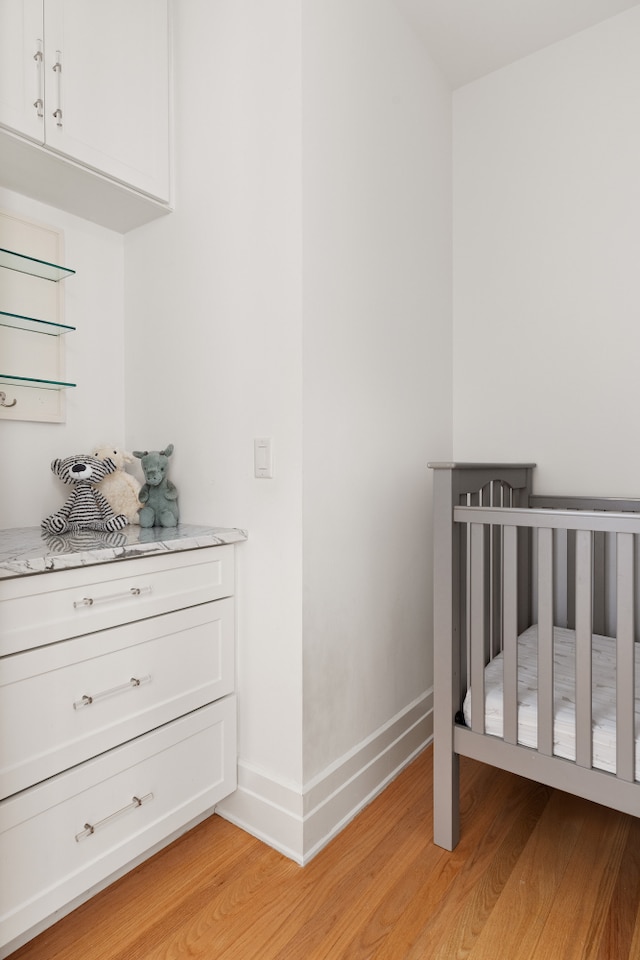 bedroom featuring light wood finished floors, a crib, and baseboards