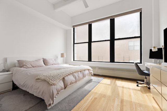bedroom with radiator heating unit, wood finished floors, beamed ceiling, a desk, and ceiling fan