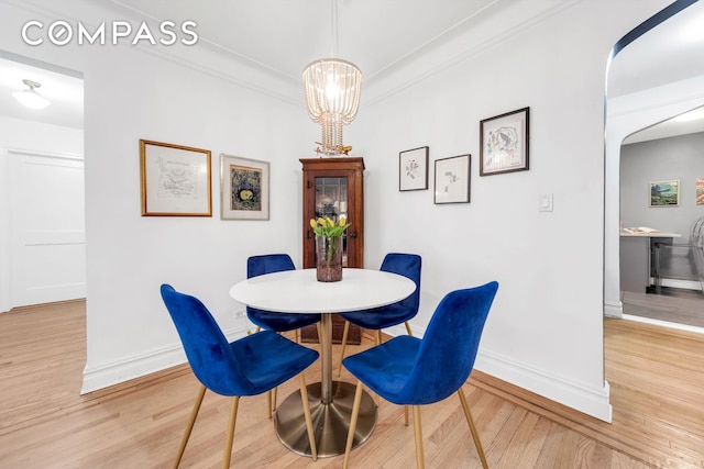 dining area featuring baseboards, light wood finished floors, a chandelier, and arched walkways