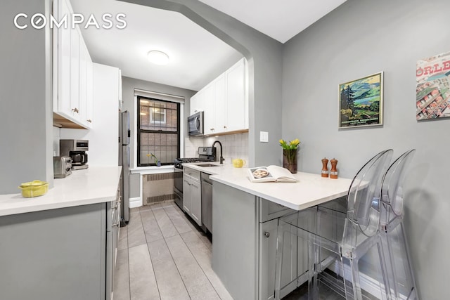 kitchen featuring a kitchen breakfast bar, appliances with stainless steel finishes, light countertops, white cabinets, and a peninsula