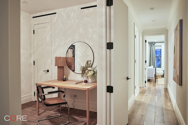 hall featuring wood finished floors, crown molding, and baseboards