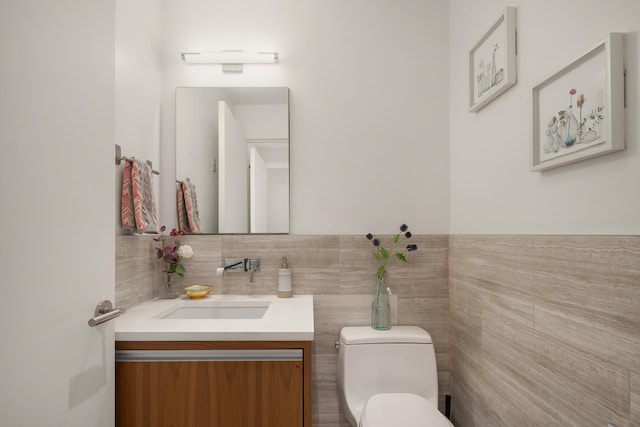 bathroom with vanity, wainscoting, toilet, and tile walls