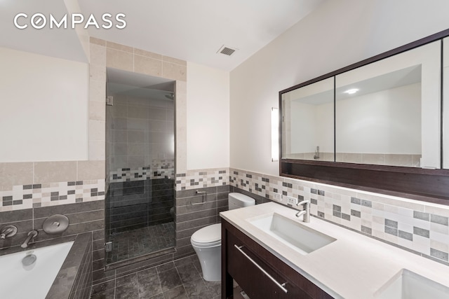 full bath with visible vents, toilet, a sink, tile walls, and a garden tub