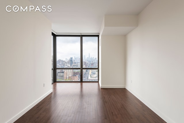 spare room with a city view, baseboards, floor to ceiling windows, and dark wood finished floors