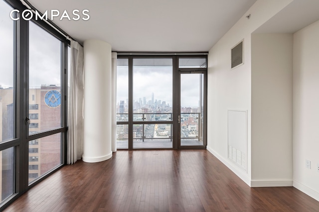 unfurnished room with floor to ceiling windows, wood finished floors, visible vents, and baseboards