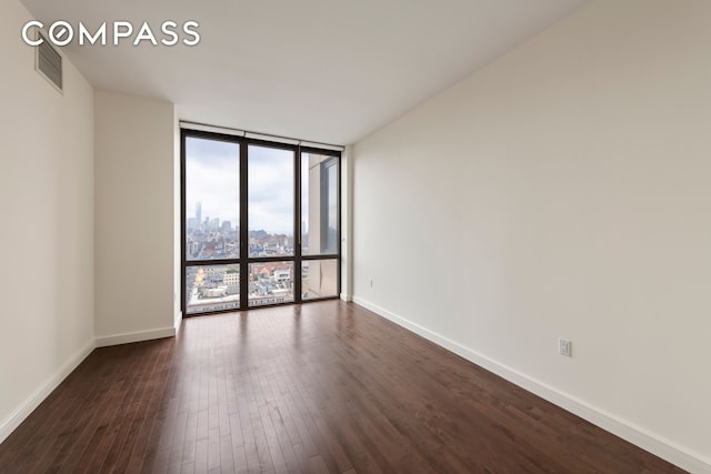 empty room featuring expansive windows, dark wood-type flooring, and visible vents