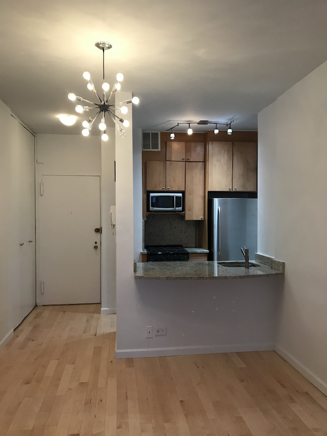 58 W 58th St Unit 9D, New York City, NY 10019 - kitchen with appliances with stainless steel finishes, a chandelier, light wood-style floors, a sink, and brown cabinetry