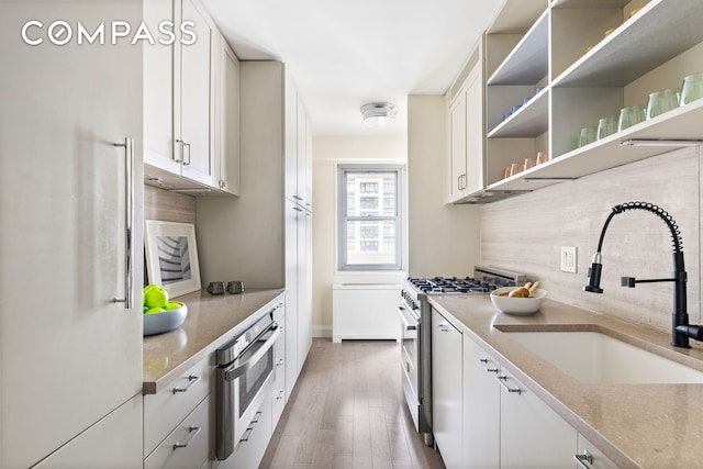 100 W 93rd St Unit 11J, New York City, NY 10025 - kitchen featuring appliances with stainless steel finishes, a sink, backsplash, light wood-style floors, and white cabinets