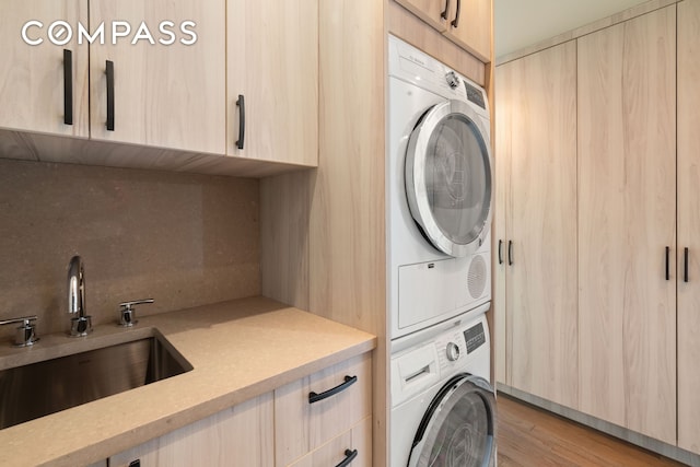 laundry area featuring stacked washer / drying machine, cabinet space, and light wood-type flooring