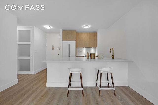 kitchen featuring a peninsula, a kitchen bar, light wood-type flooring, light countertops, and white refrigerator