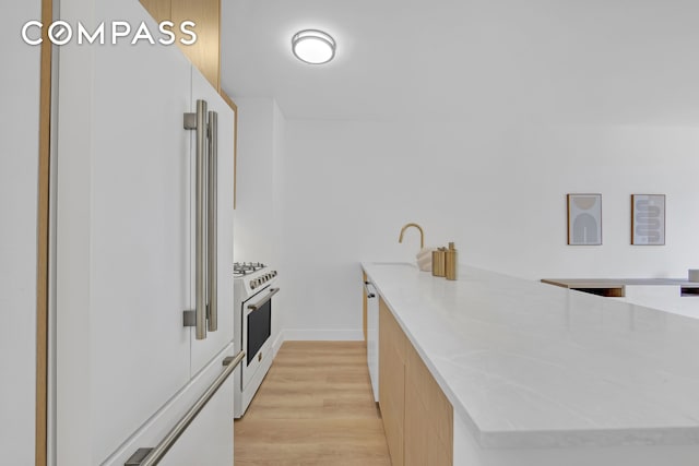 kitchen with a peninsula, white appliances, modern cabinets, a sink, and light wood finished floors