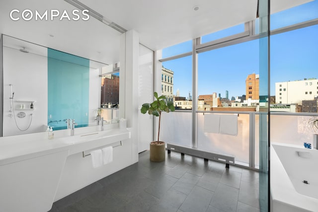 bathroom with a view of city, tile patterned flooring, floor to ceiling windows, a freestanding bath, and a sink