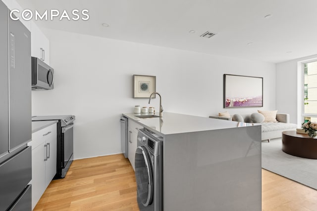 40 Schaefer St Unit 3R, New York City, NY 11207 - kitchen featuring washer / dryer, a peninsula, light wood-style floors, a sink, and stainless steel appliances